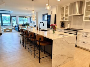 Una cocina moderna con una isla de mármol, taburetes de bar y vistas al exterior.