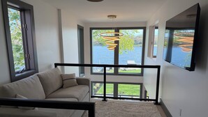 A modern interior with a sofa, large windows, and a hanging light fixture. - The Lakehouse on Mona Lake (Norton Shores)