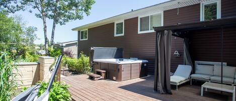 A deck with a hot tub, outdoor seating, and a pergola.