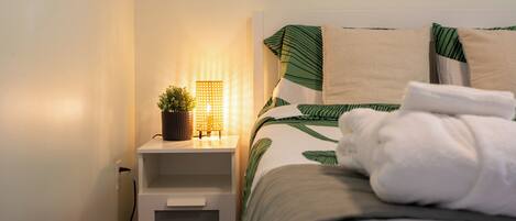 A neatly made bed with a green leaf pattern, a bedside lamp, and a small potted plant on the nightstand.