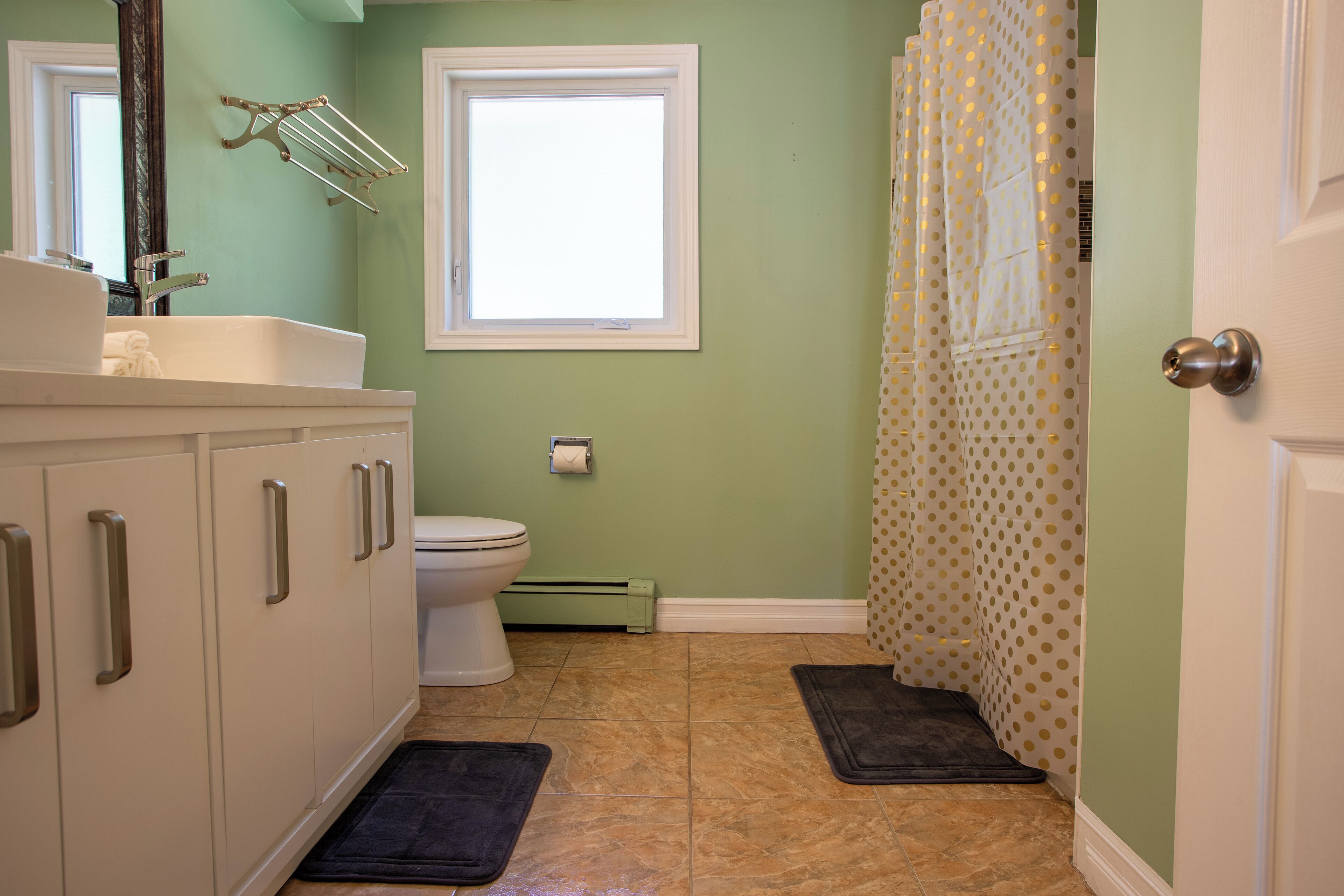 A bathroom with a white sink, a toilet, a window, and a shower curtain with a polka dot pattern.