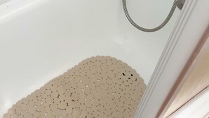 Eine Badewanne mit Duschschlauch und einer beigen Badematte.