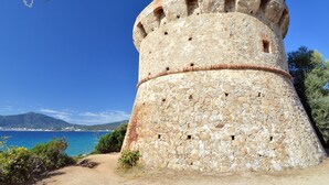 Ein historischer Stein-Turm mit kreisförmigem Fundament und Zinnen, mit Blick auf eine Küstenlandschaft.