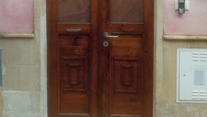 A wooden double door with a keyhole and a handle, set in a pink wall with a metal vent below.