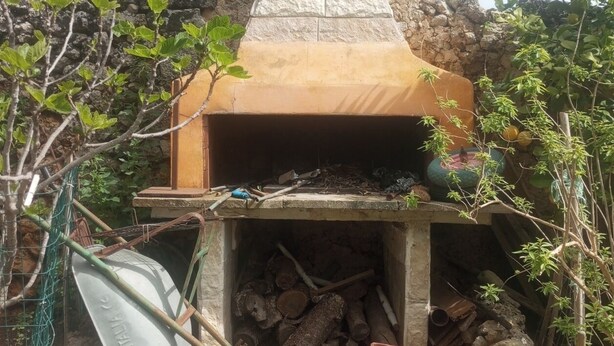 A stone-built outdoor oven with a chimney, surrounded by vegetation and construction materials.