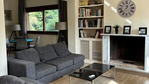 Uma sala de estar com sofá, mesa de centro, estante, lareira e um relógio de parede grande.