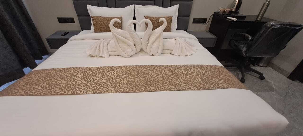 A neatly made bed with a leopard print throw, two pillows, and a swan-shaped towel arrangement.