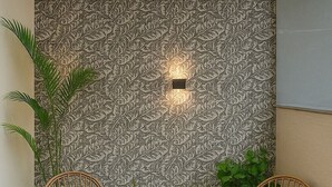 A corner with two wicker chairs, a patterned wall, and potted plants. - Inn Of Joy (Noida)