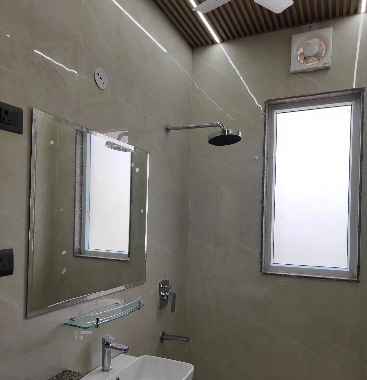Une salle de bain moderne avec une douche à l’italienne en verre, un grand miroir et une fenêtre.