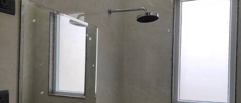 Un baño moderno con cabina de ducha de vidrio, un espejo grande y una ventana.
