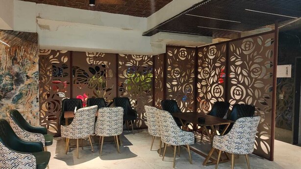 A modern indoor seating area with patterned chairs and a ceiling fan. - Inn Of Joy (Noida)