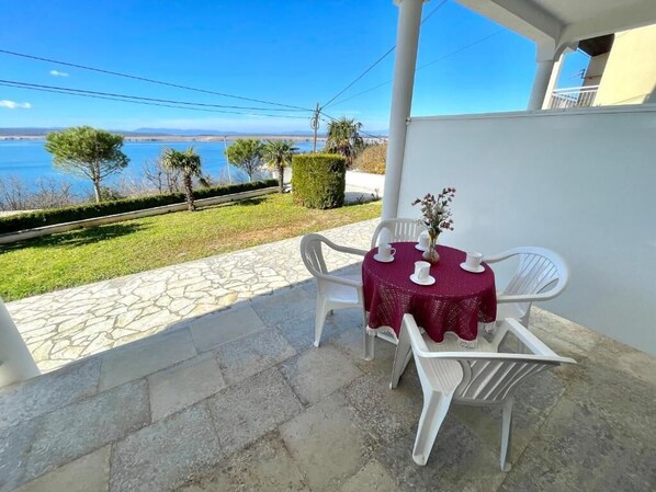 Une terrasse avec une table et des chaises, une vue sur la mer et un bâtiment blanc.