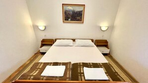 Una cama pequeña y bien hecha con cabecera de madera, dos mesitas de noche y un cuadro en la pared.