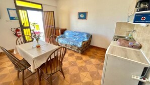 Una habitación compacta con una mesa de comedor, sillas, un sofá, un refrigerador y una pequeña cocina.