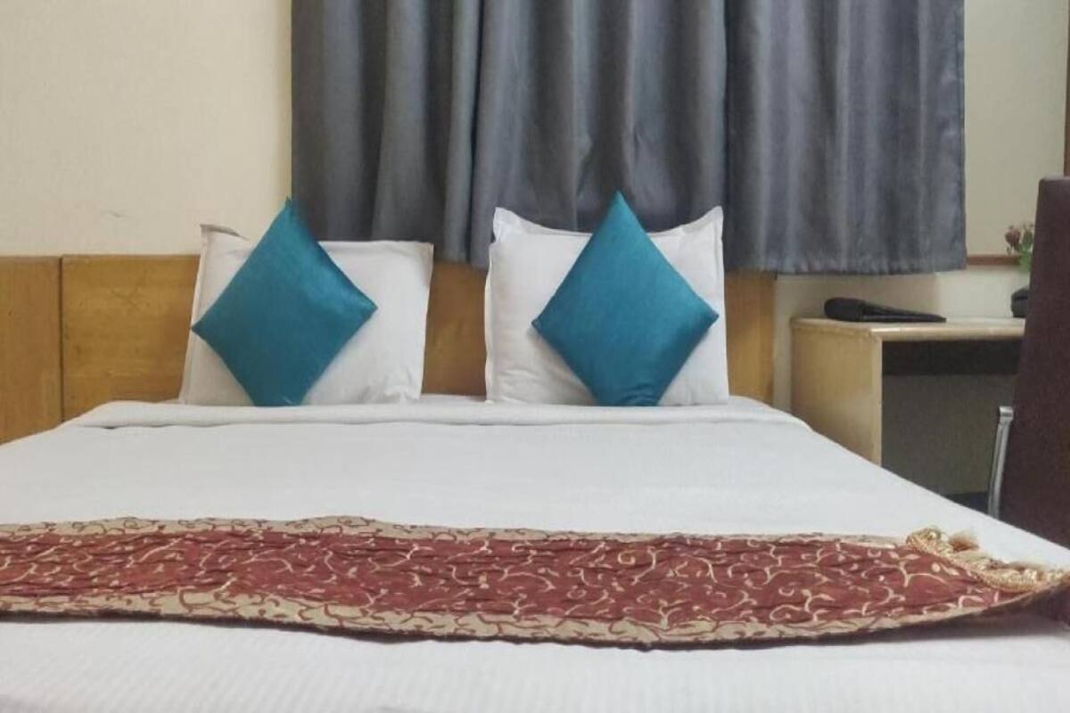 Una habitación de hotel con cama, dos almohadas, una manta, una mesita de noche y una silla.