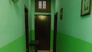 Un couloir aux murs verts et au sol carrelé, qui mène à une porte sombre au fond.
