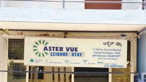 L’entrée d’un hôtel, avec une enseigne indiquant « Aster Vue Leisure Stay », et proposant des services tels que l’hébergement de longue durée, la formule « chambre et petit-déjeuner », la climatisation et le Wi-Fi gratuit.