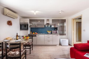 A modern kitchen with a central island, built-in appliances, and a dining area with a red sofa. - The Wave - Apt With Seaview and Garden (Kostrena)