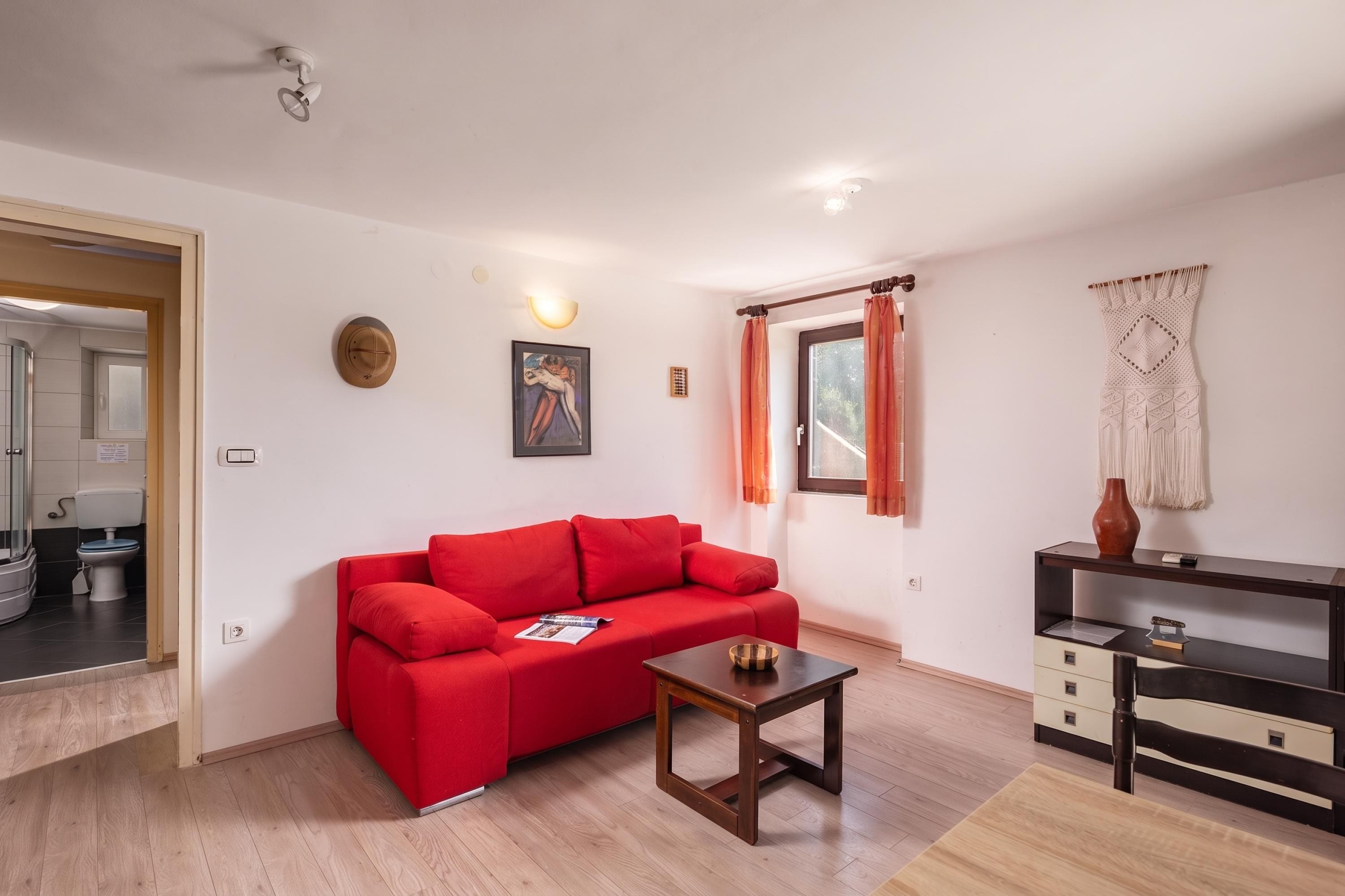 Uma sala de estar moderna com um sofá vermelho, uma mesa de centro de madeira e uma janela com cortinas.