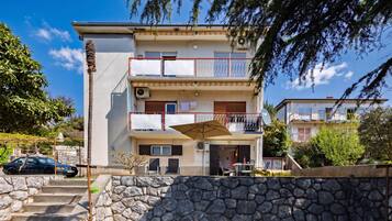 A multi-story residential building with balconies, a stone wall in front, and a parked car.