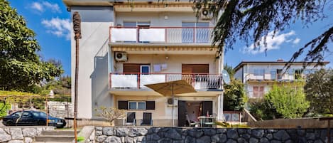 A multi-story residential building with balconies, a stone wall in front, and a parked car.
