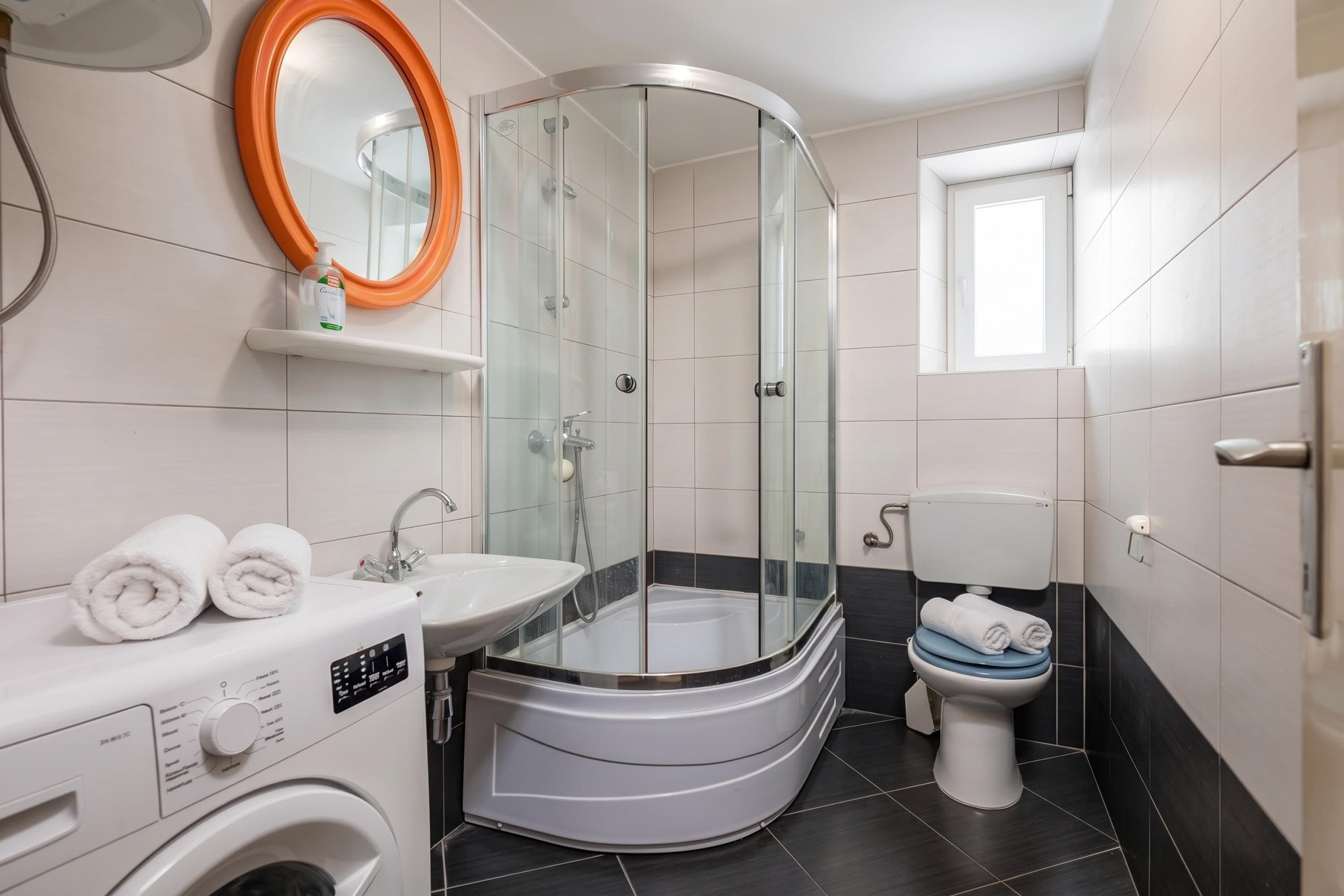 A modern bathroom with a glass-enclosed shower, a white sink, a toilet, and a washing machine.