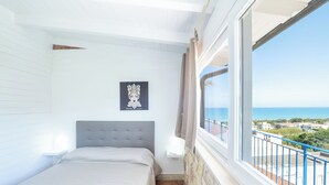 A bedroom with a bed, a window with a view of the sea, and a picture on the wall.