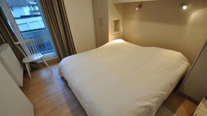 A bedroom with a large bed, a chair, and a window with curtains. - Apartment in Duinbergen With Side Sea View (Knokke-Heist)