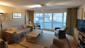 A modern living room with a sofa, armchairs, a coffee table, and a TV. - Apartment in Duinbergen With Side Sea View (Knokke-Heist)