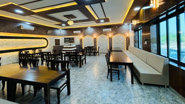 A restaurant with marble flooring, wooden tables and chairs, a bar area, and large windows offering a view. - Hotel Shri Tulsi Residency (Phalodi)
