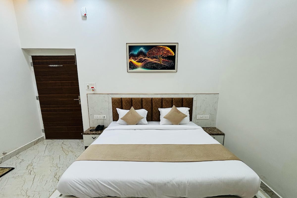 Une chambre d’hôtel avec un grand lit, une tête de lit dotée de panneaux verticaux, deux tables de chevet, une commode, une porte et un tableau encadré au mur.