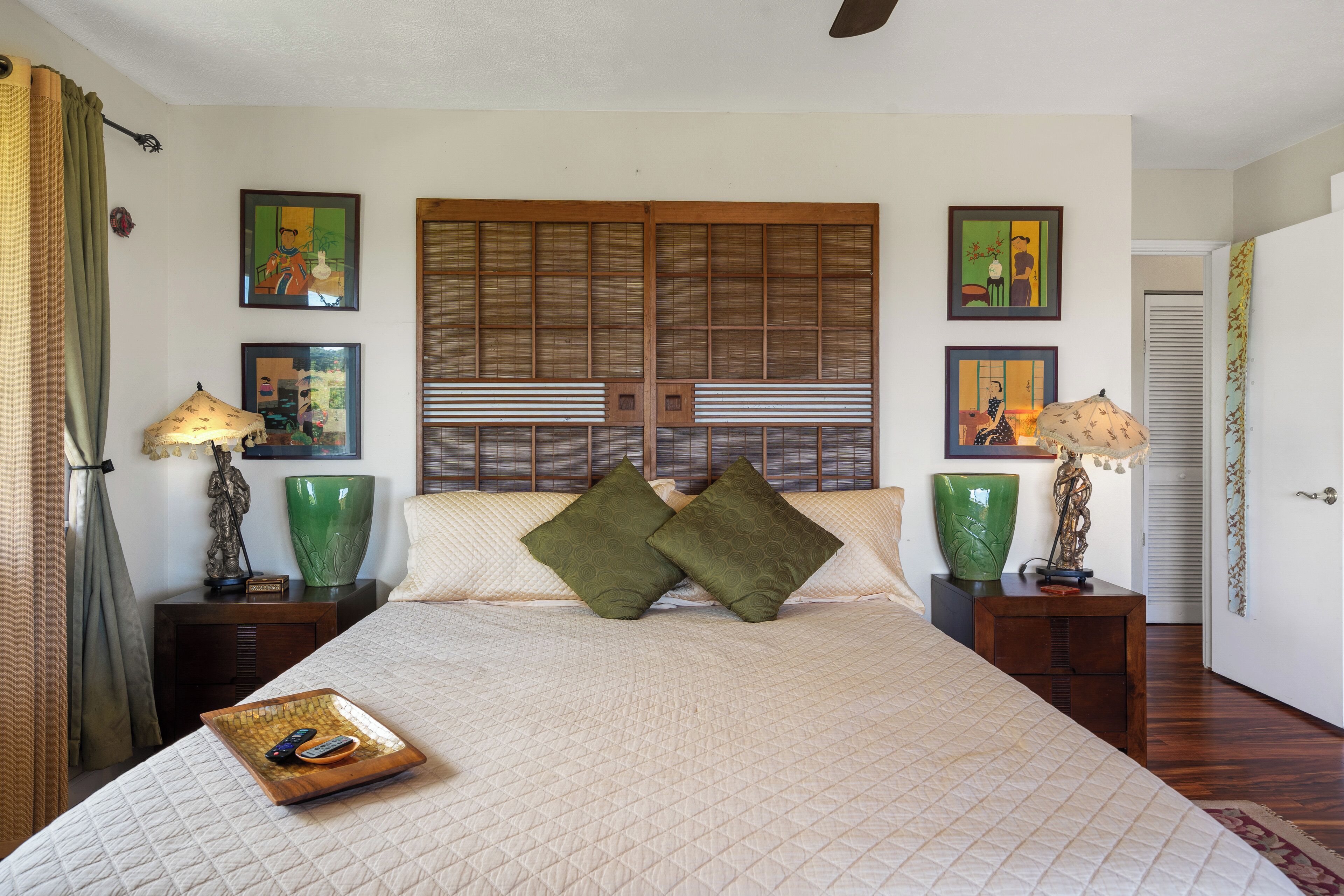 A neatly arranged bedroom with a large bed, two nightstands, a green vase, and framed artwork on the walls.