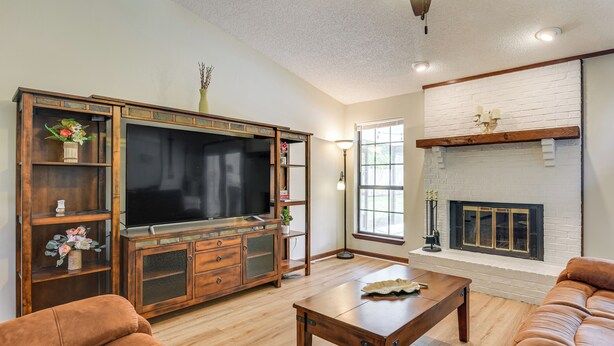 A living room with a large flat-screen TV, wooden entertainment center, brown leather sofa, and a fireplace. - Private Pool & Patio: Niceville Family Home (Niceville)