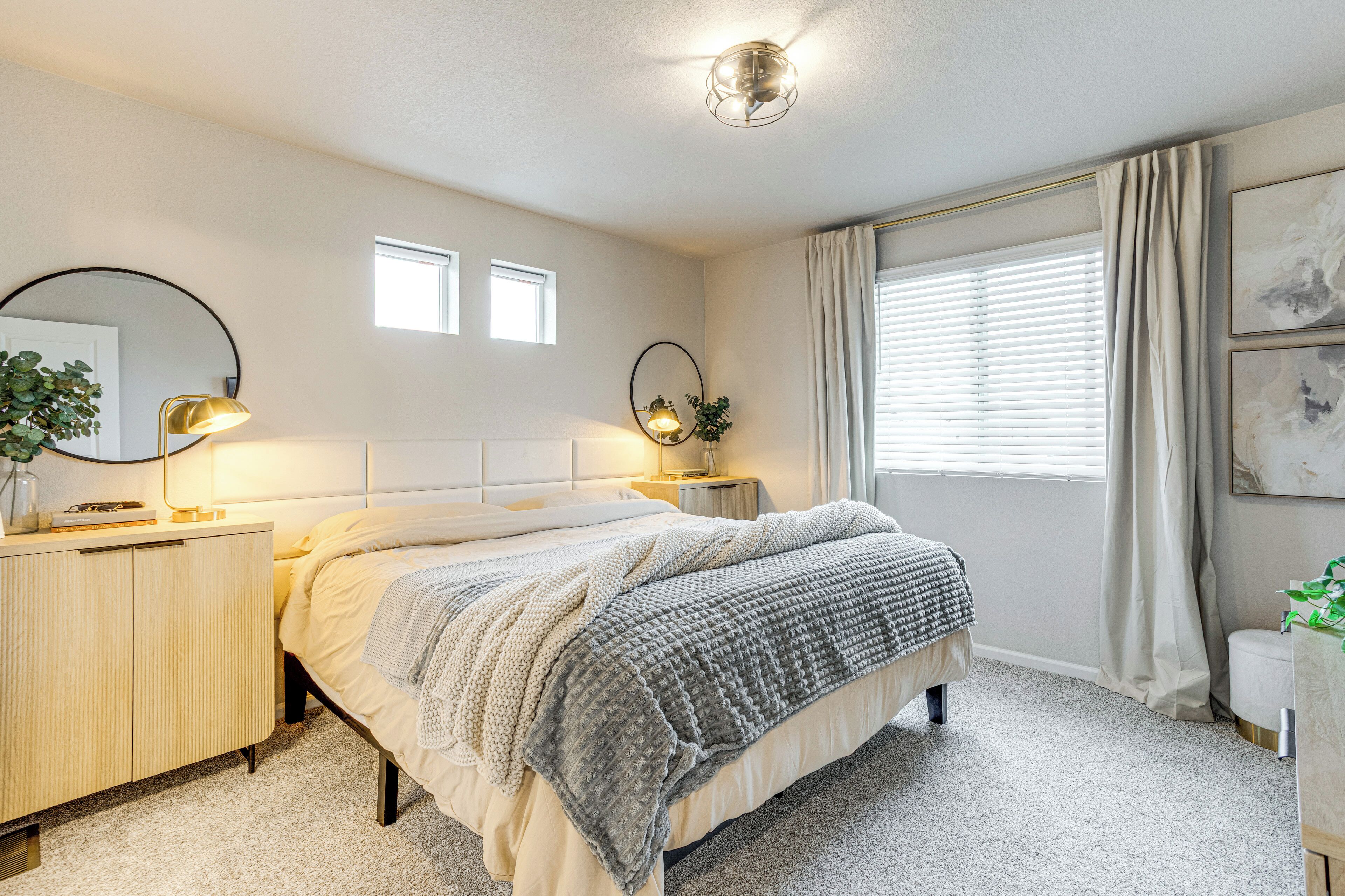 A bedroom with a bed, bedside tables, a mirror, and a window with curtains.