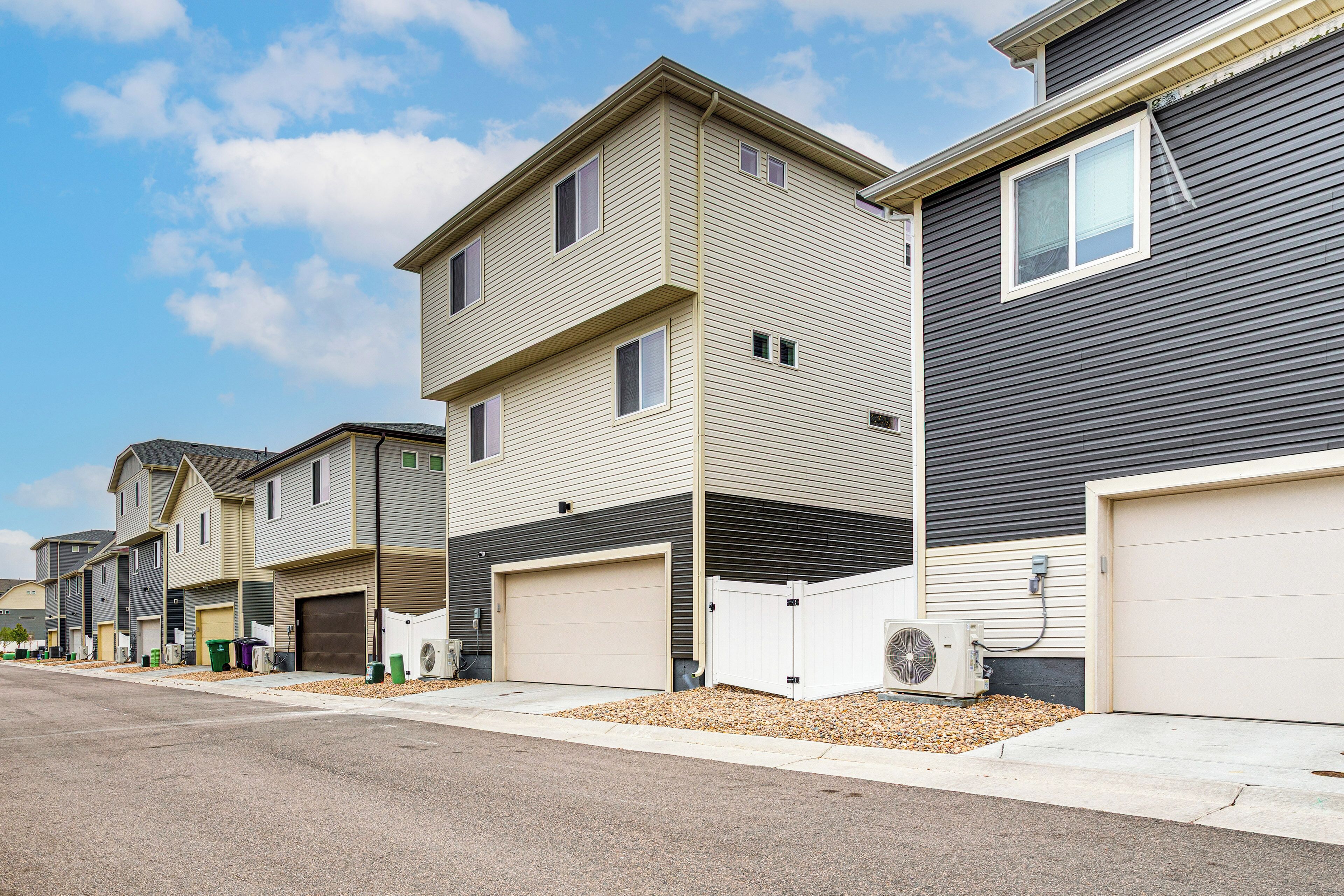 A row of townhouses with attached garages, a clear sky, and a gravel driveway.