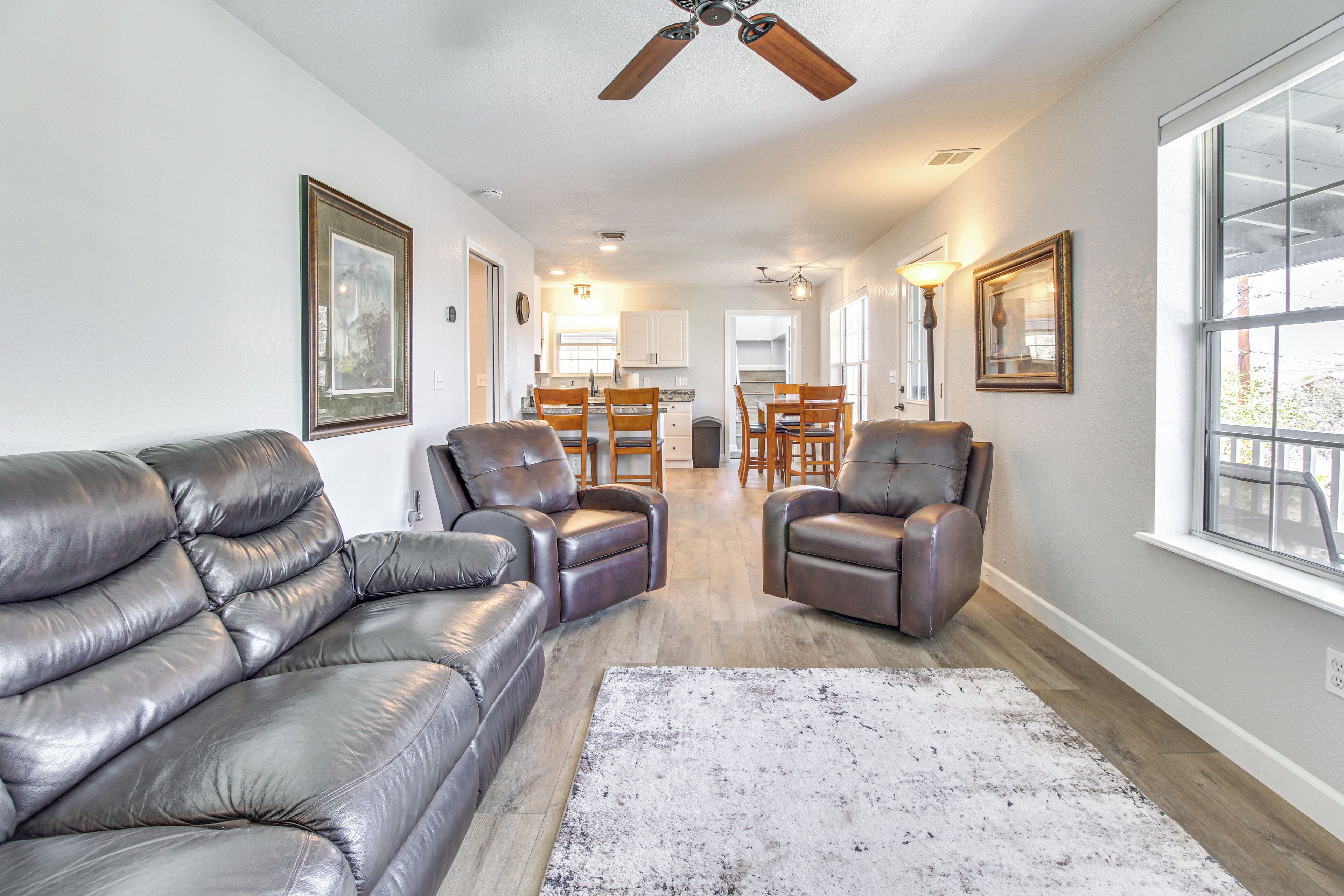 A spacious living room with leather sofas, a dining area with wooden chairs, and a kitchen in the background.