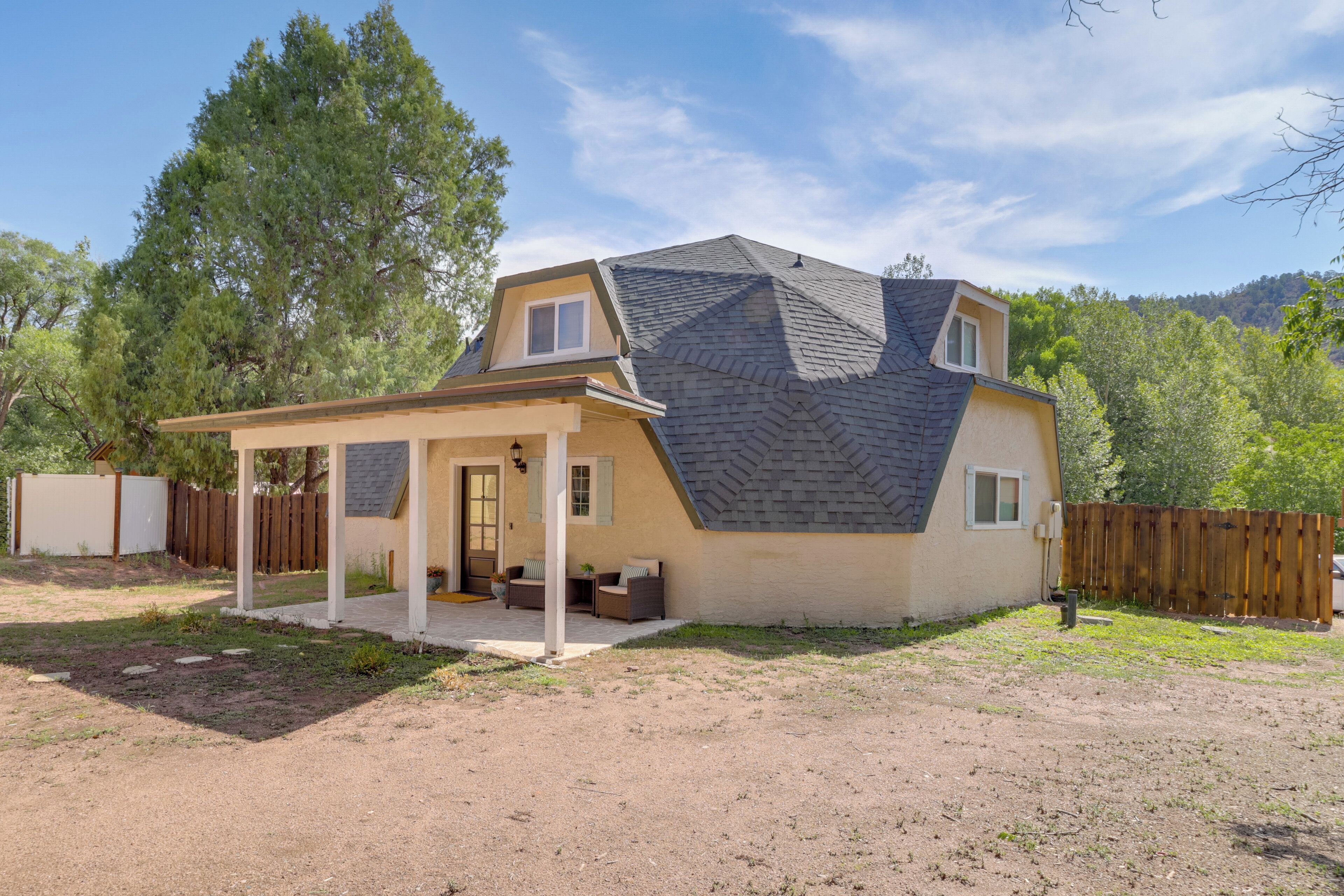 A two-story house with a covered patio, a fenced yard, and a large tree in the background.