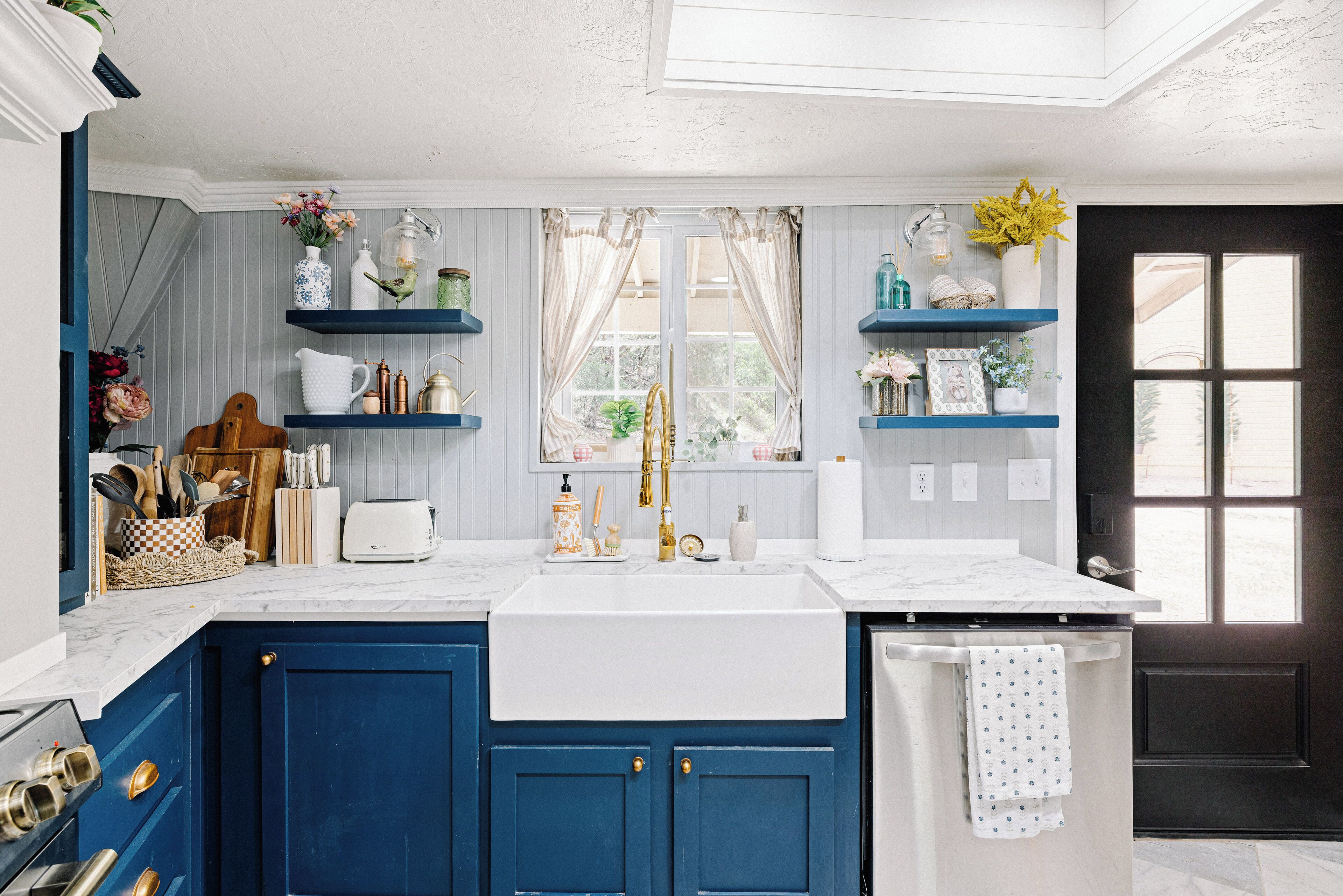 A kitchen with blue cabinets, a white sink, and a window with curtains.