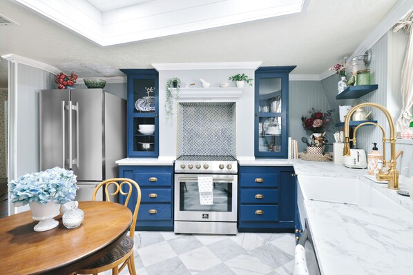 A modern kitchen with blue cabinets, a stainless steel refrigerator, a built-in oven, and a white countertop.