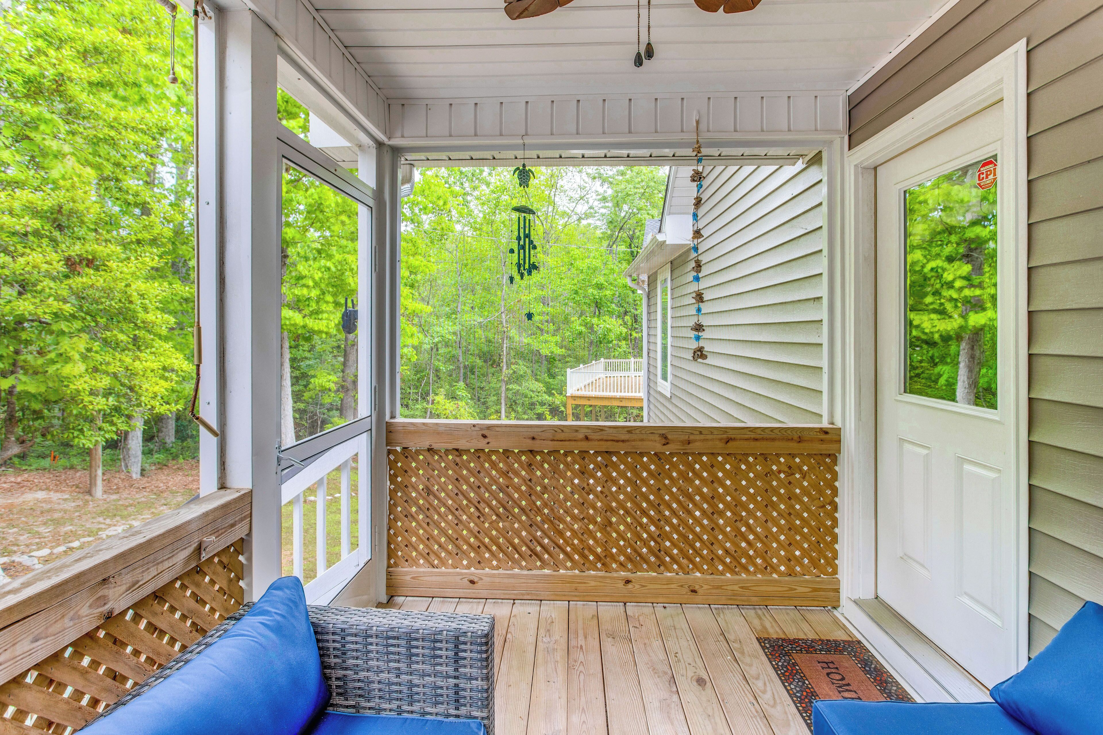 A covered porch with a wooden deck, a bench with blue cushions, and a view of a wooden deck and trees.