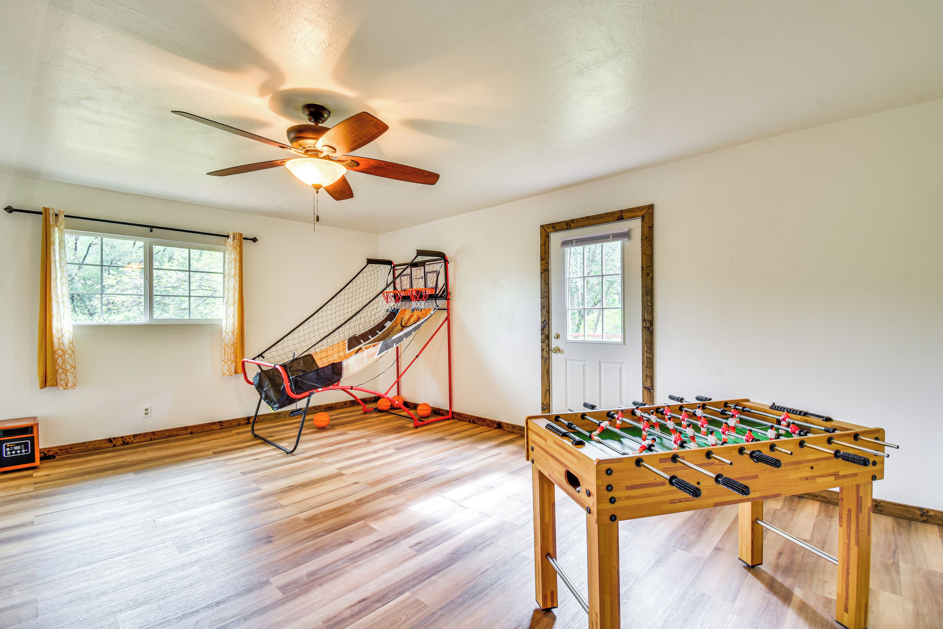 Une pièce avec un plancher en bois, un ventilateur de plafond, une table de baby-foot et un hamac.
