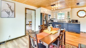 Une cuisine moderne avec des meubles en bois, des appareils électroménagers en acier inoxydable et un coin repas comprenant une table et des chaises en bois.