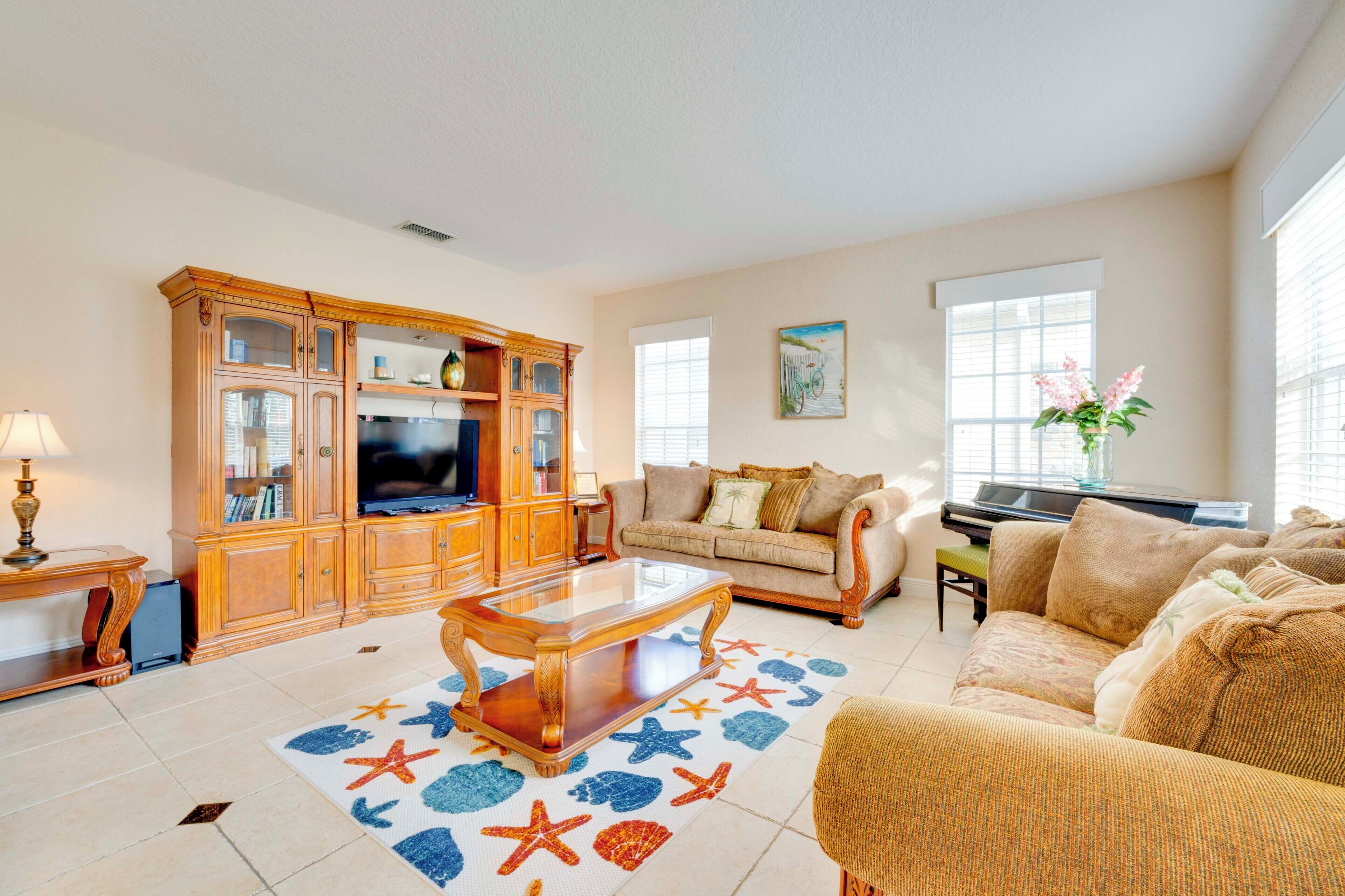 A spacious living room with a wooden entertainment center, a large flat-screen TV, a beige sofa, and a coffee table with a starfish rug.