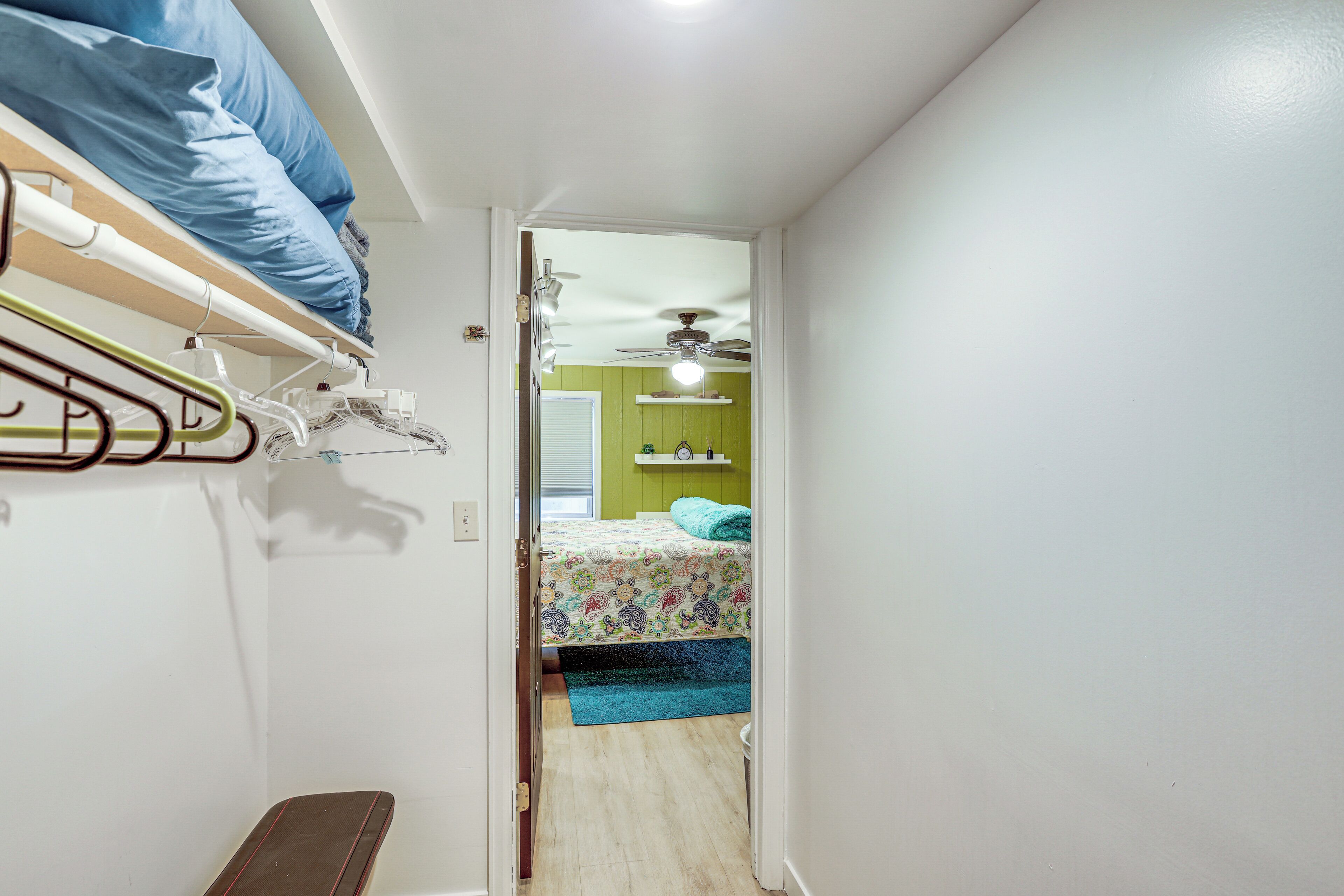 Ein schmaler Flur führt zu einem Schlafzimmer mit Bett, Deckenventilator und grüner Wand.