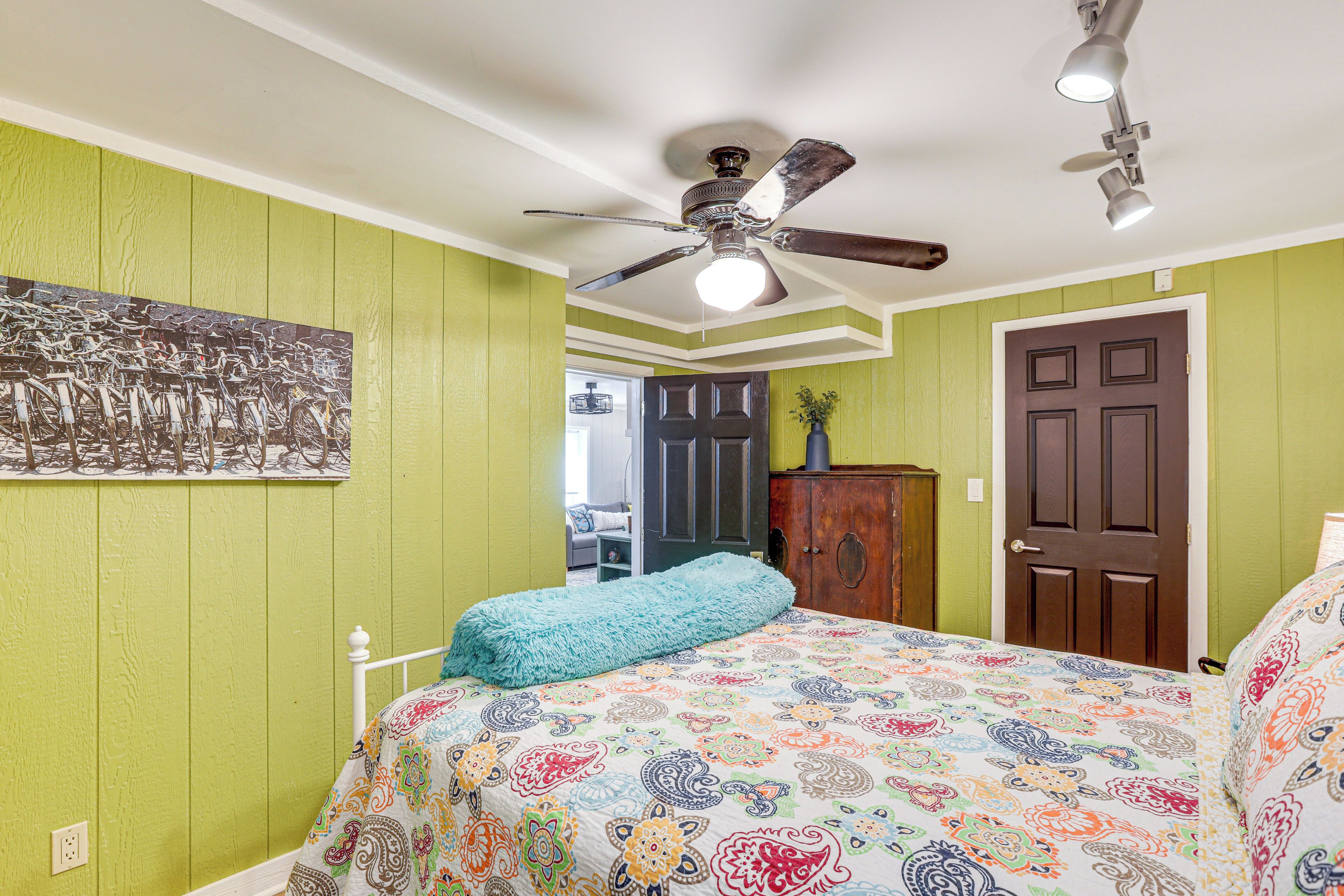 A bedroom with a bed, a ceiling fan, a door, and a wall-mounted painting.