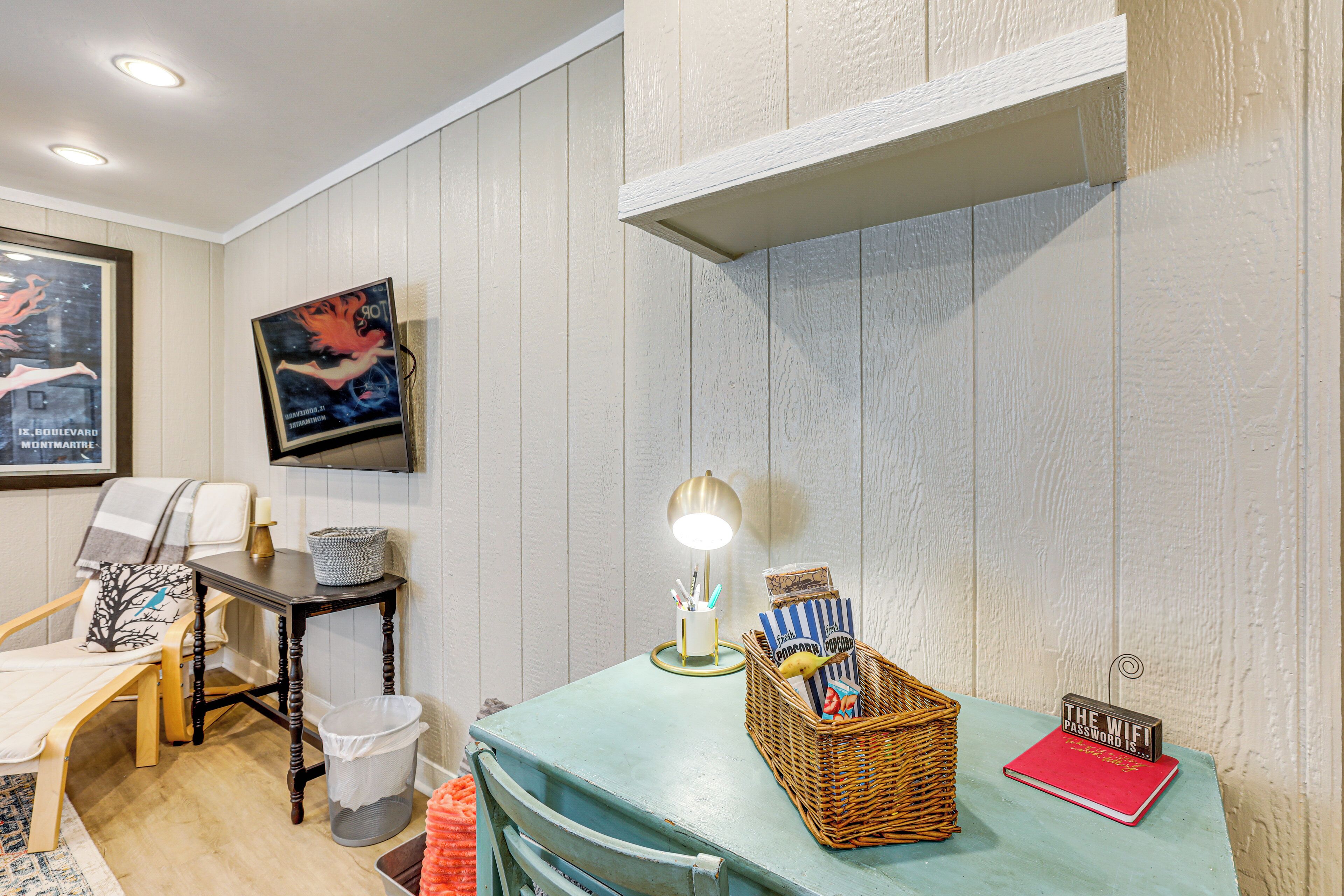 Una habitación con una mesa color turquesa, una cesta de mimbre, un libro rojo y un letrero en la pared.