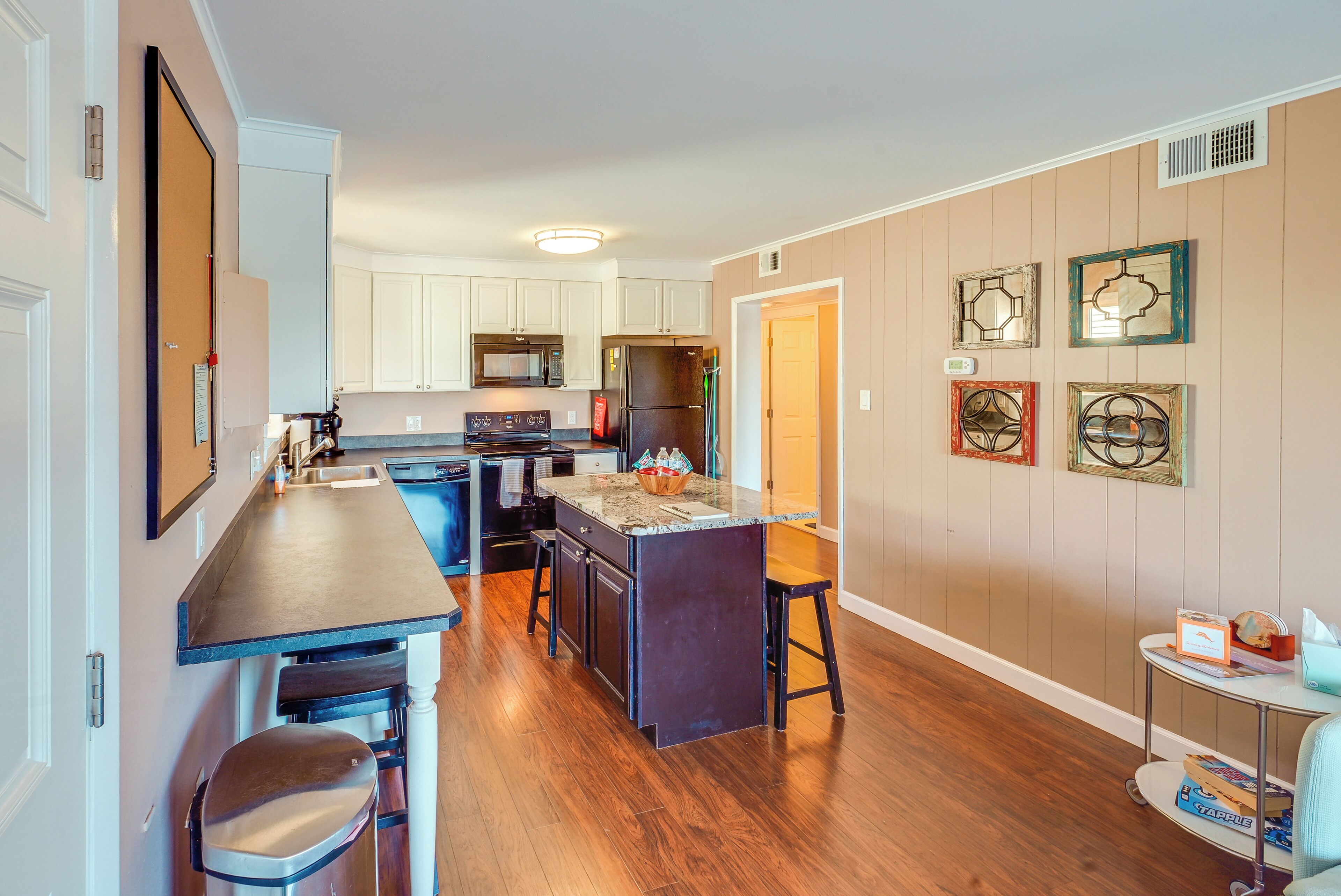 A modern kitchen with a central island, white cabinets, and a wooden floor.