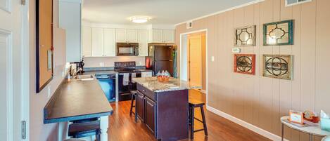 A modern kitchen with a central island, white cabinets, and a wooden floor.