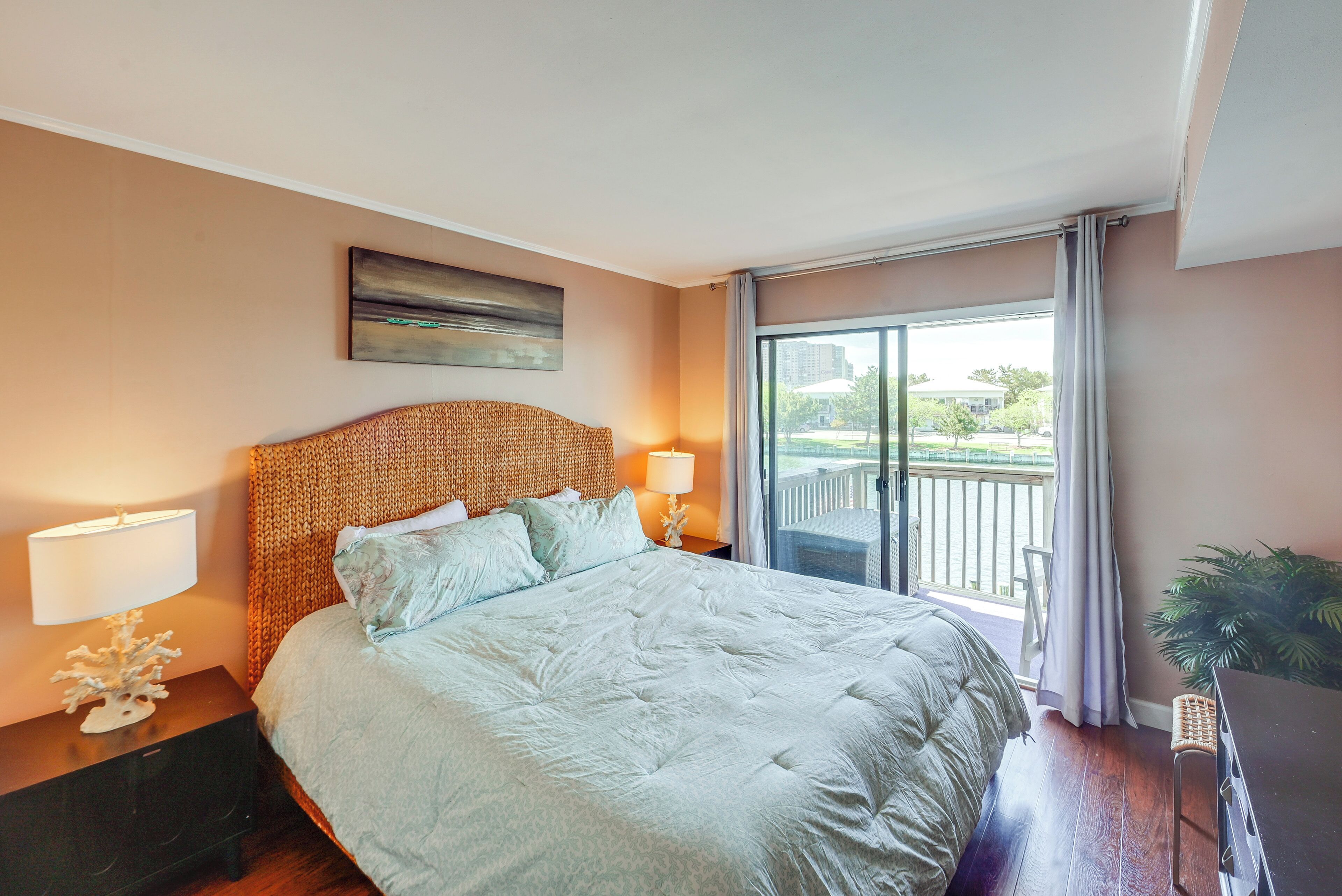 Une chambre d’hôtel avec un grand lit, une table de chevet avec une lampe, un tableau au mur et une vue sur l’extérieur par une porte coulissante.
