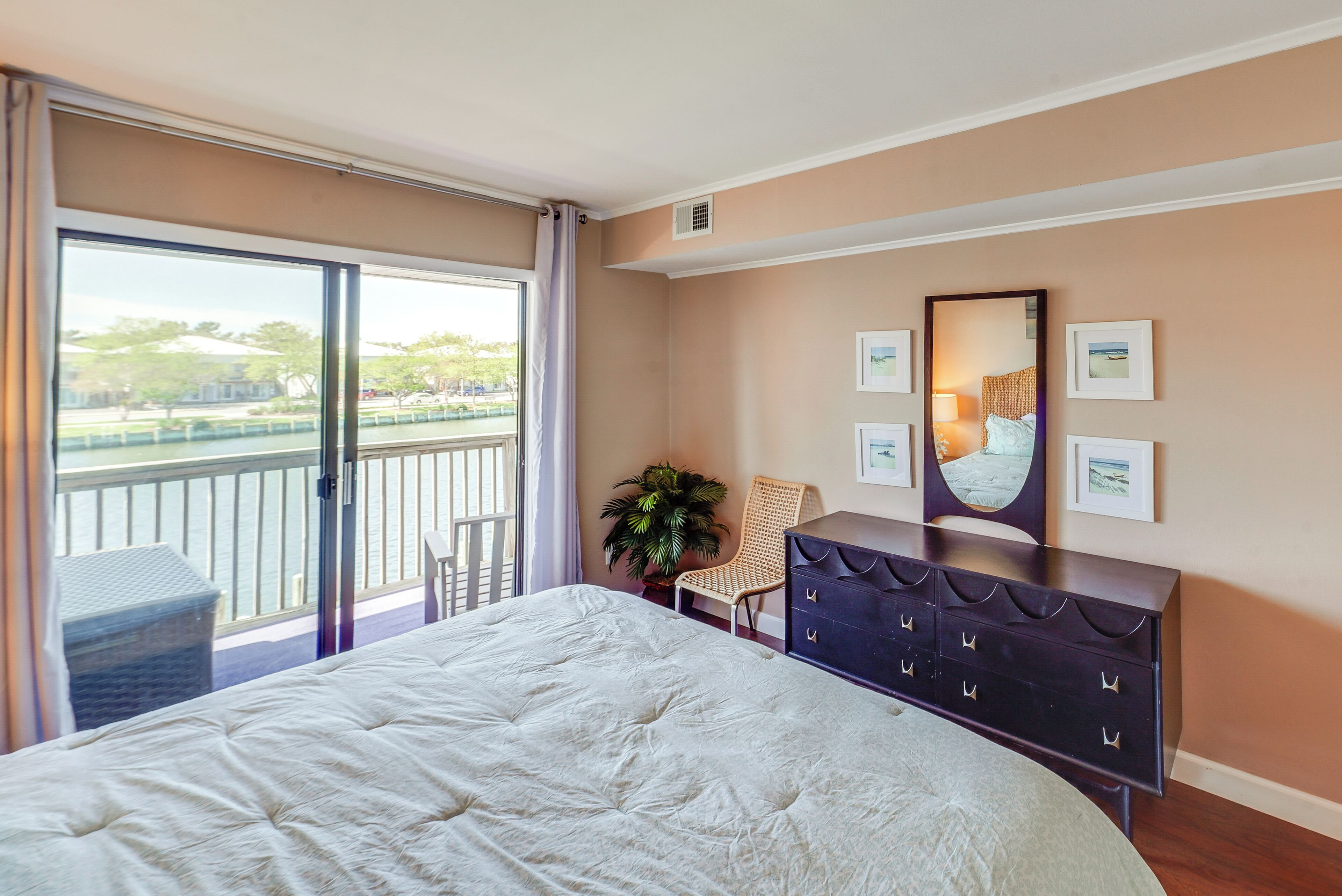 A bedroom with a large bed, a dresser, a chair, and a balcony with a view of the outdoors.